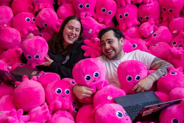 Two Octopus Energy team members laughing among a pile of pink octopus plush toys